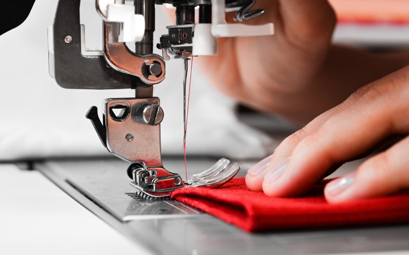 Close-up of two hands working with a sewing machine on a straight stitching setting, sewing a red piece of fabric.
