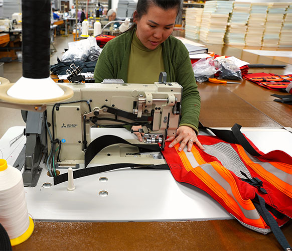 crane operator orange & red vest being sewn on industrial sewing machine by LJ design team member