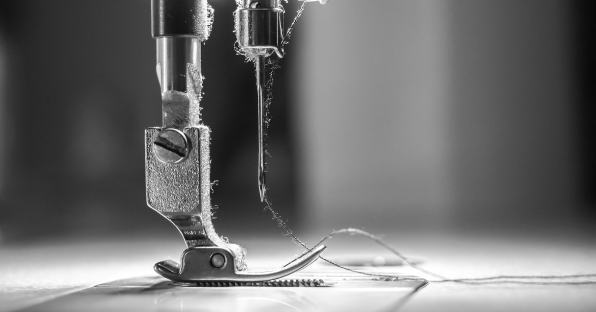 Black-and-white close-up of a sewing machine needle and presser foot stitching fabric, highlighting precision and craftsmanship.